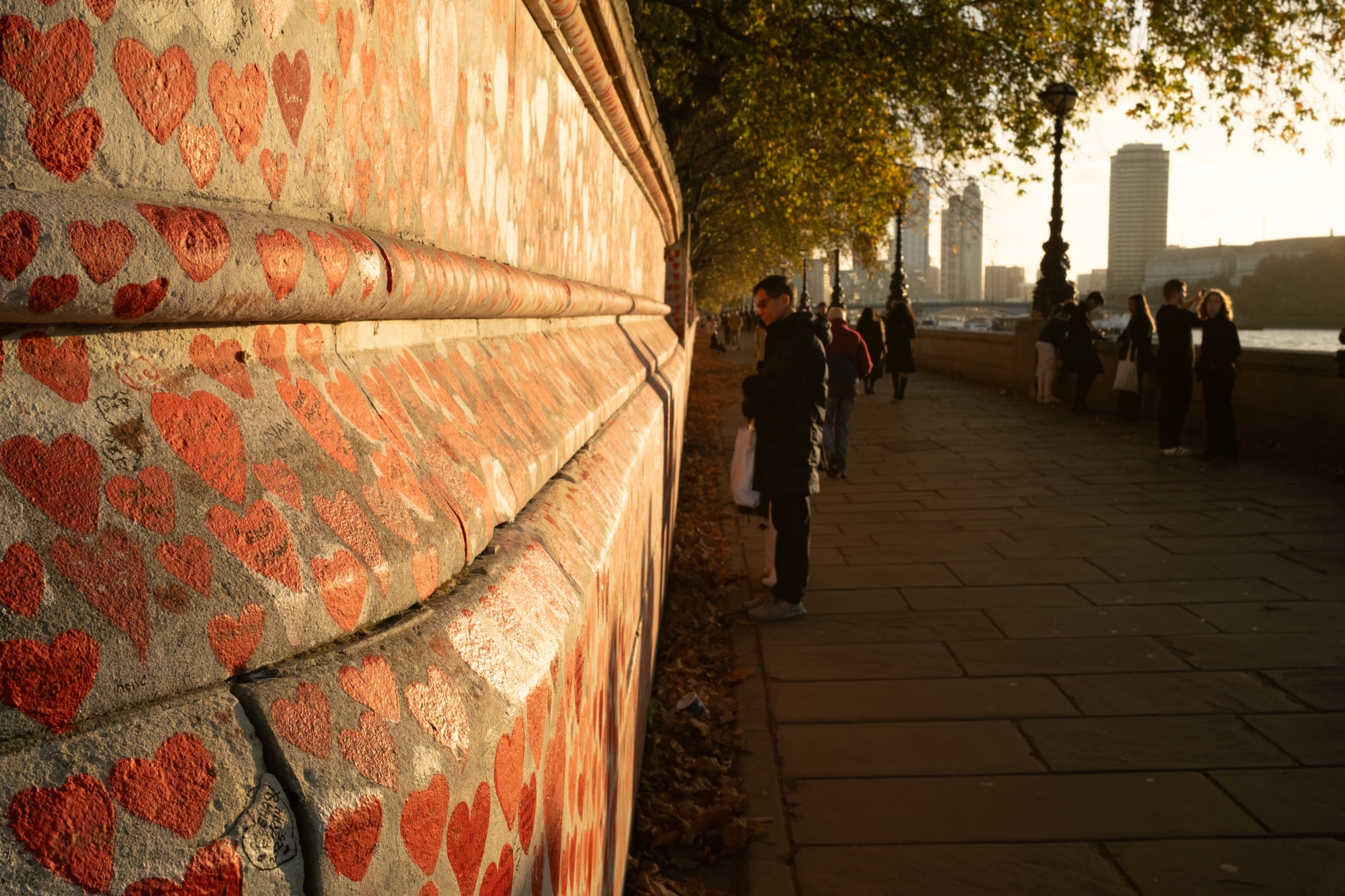 Un long mur couvert de cœurs rouges peints borde la promenade au bord de la Tamise, éclairée par le soleil bas d'automne.