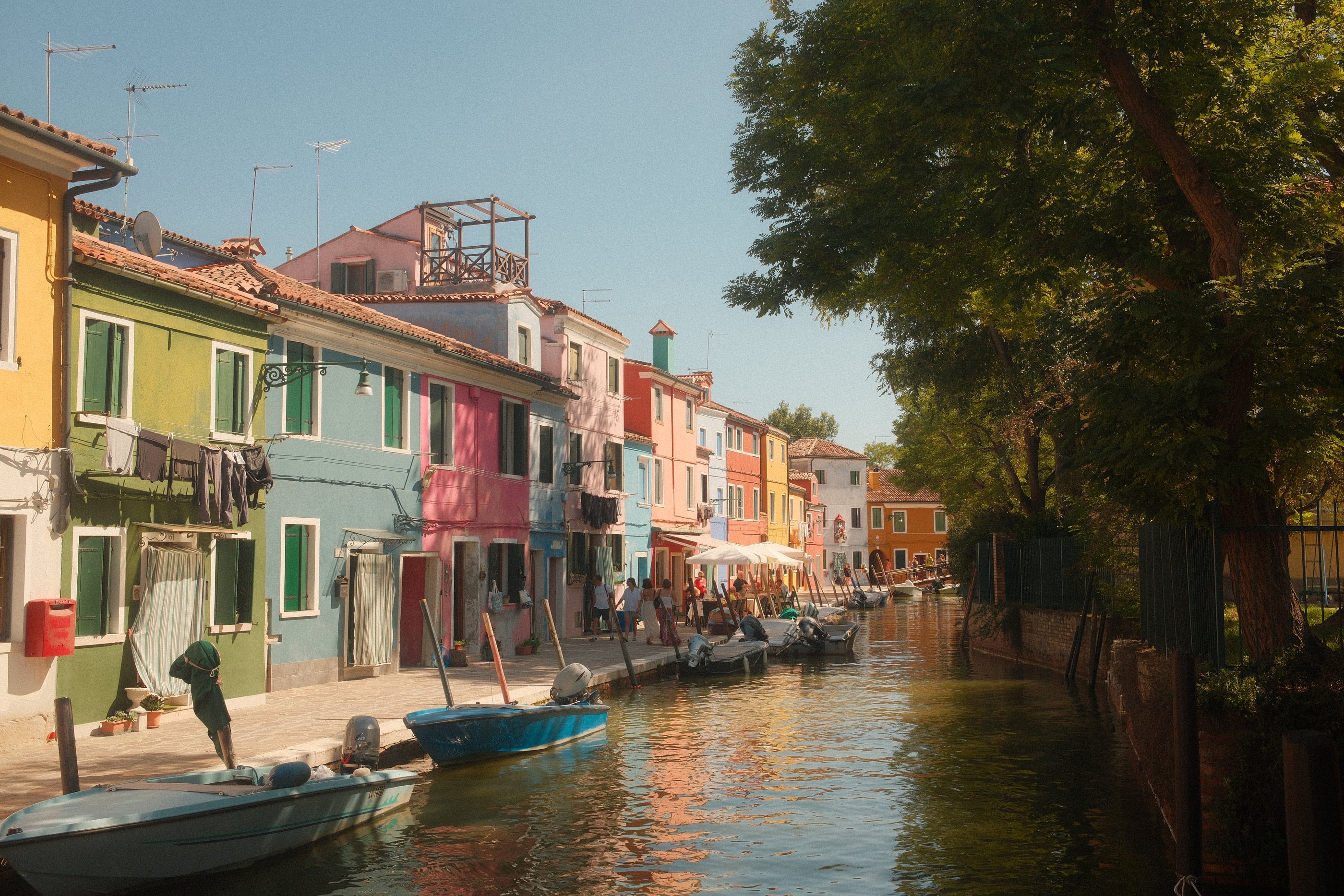 Un canal bordé de maisons multicolores et de barques, du linge aux fenêtres, de grands arbres sur l'autre rive.