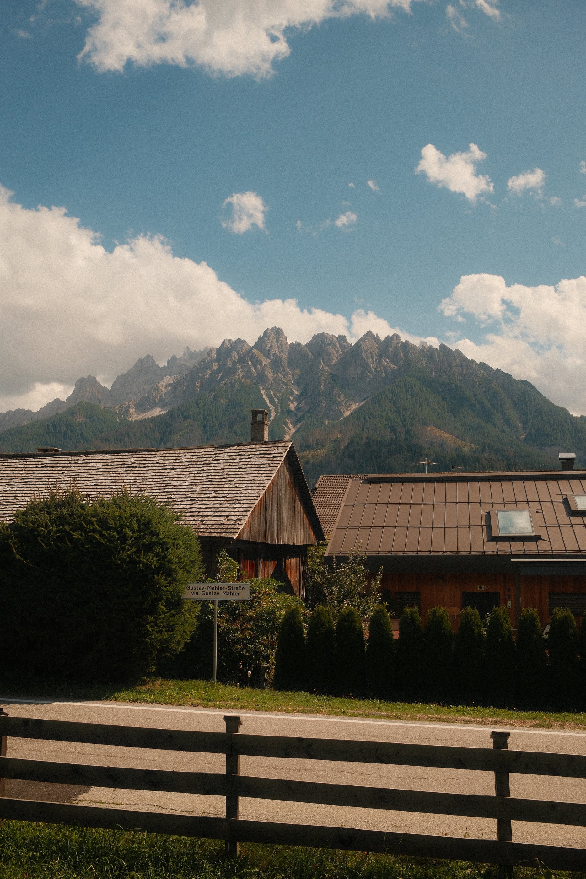 Toits de chalets en bois derrière une barrière, une chaîne de sommets dentelés sous des nuages blancs.